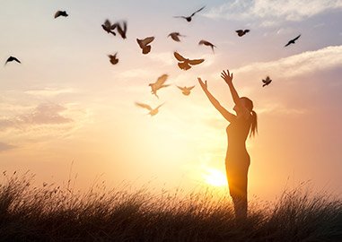 Women standing outside with arms in the air while birds are flying